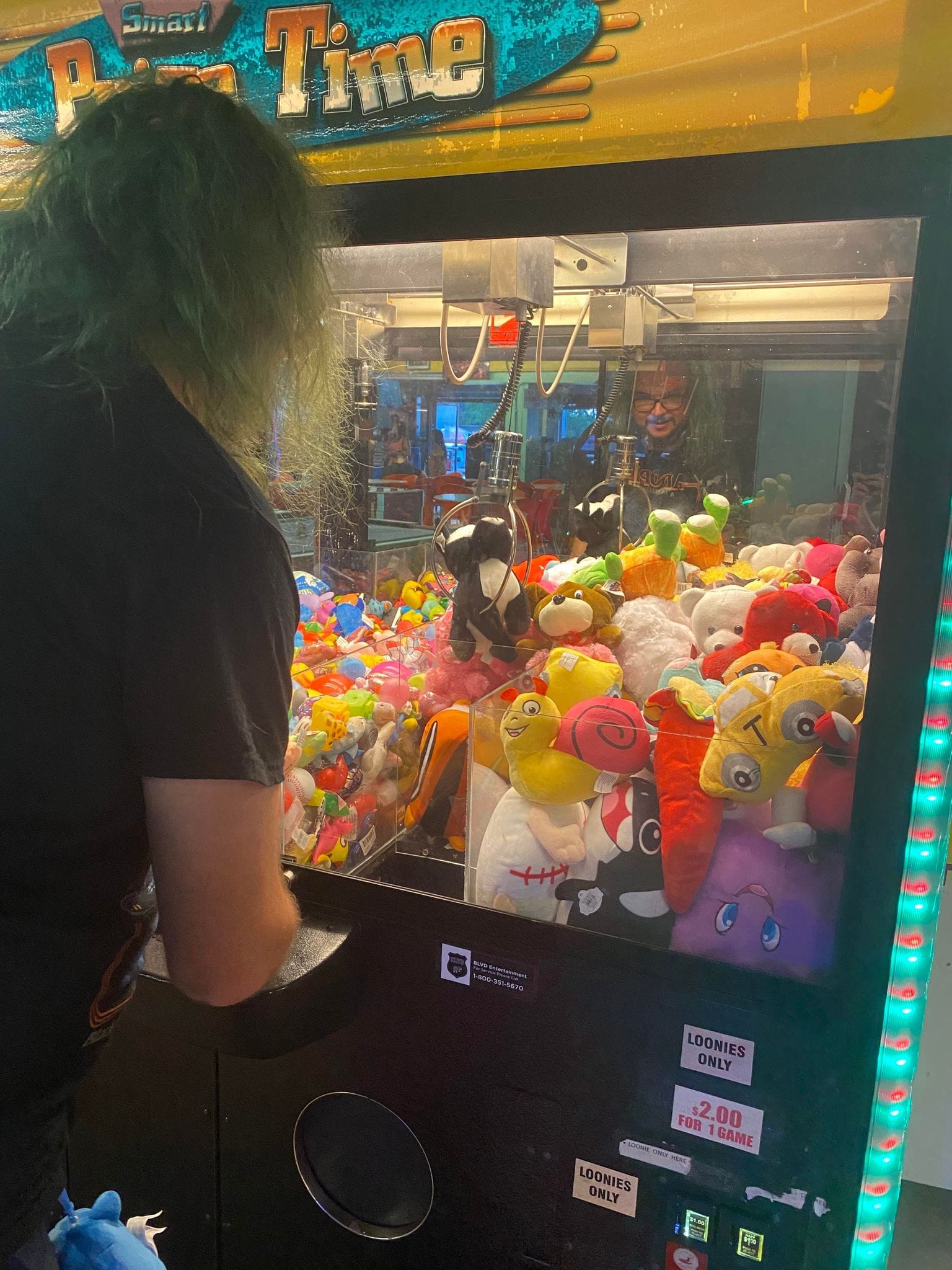 A man with green hair plays an arcade claw game, Photo 3